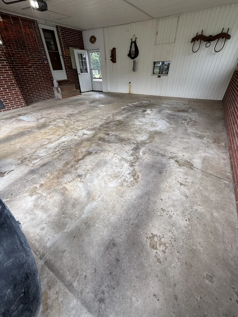 Before — Existing garage floor showing discoloration and repair needs near the entry door in Wytheville.