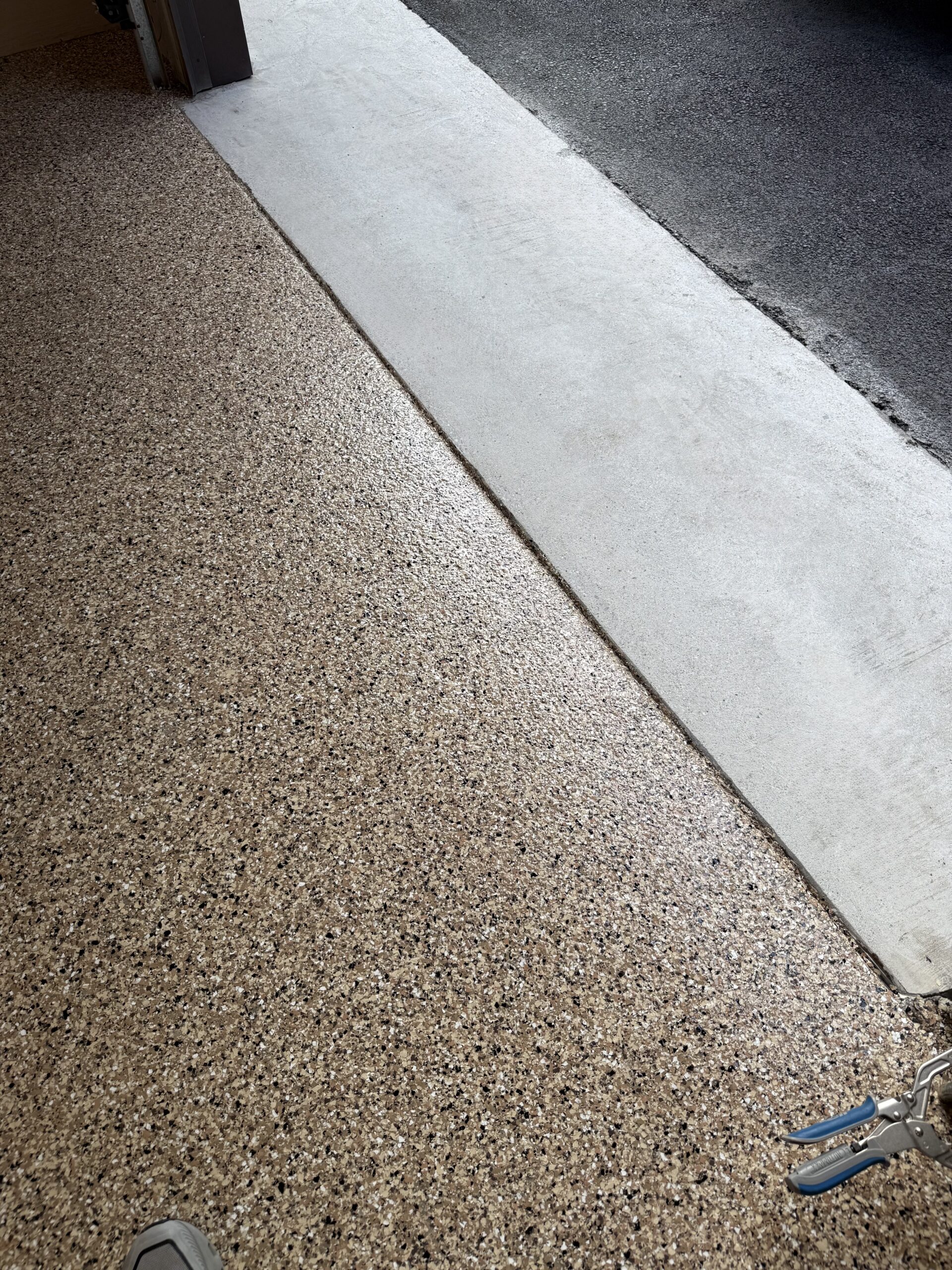 Tan decorative-flake garage floor beside the concrete apron at the doorway